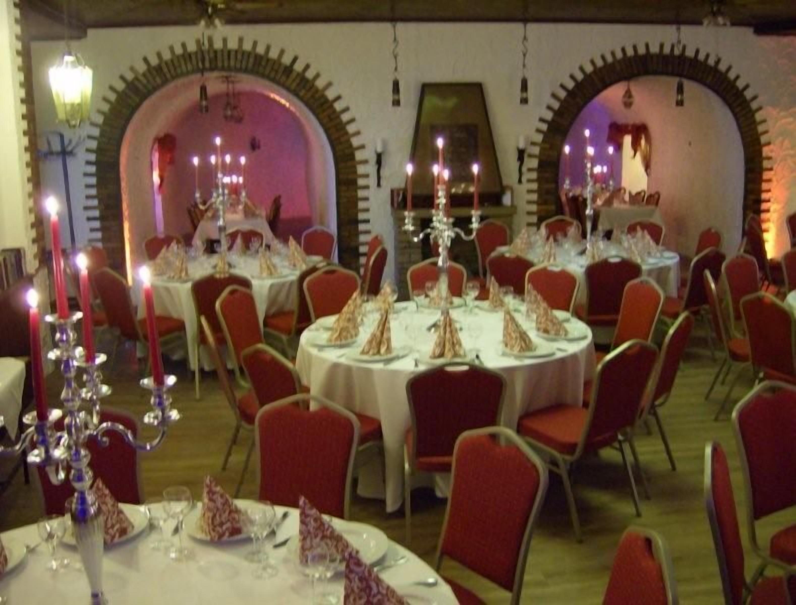 A dining area with round tables, red chairs, and candle-lit centerpieces.