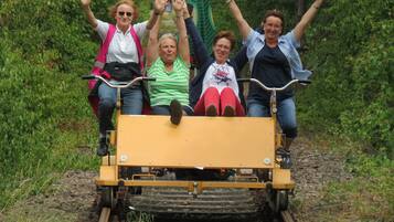 A group of people on a yellow vehicle moving along a railway track surrounded by greenery.