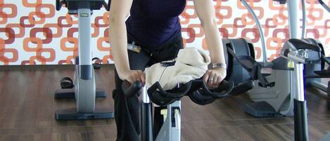 Una persona usando una máquina elíptica en un gimnasio con papel tapiz estampado y suelo de madera.