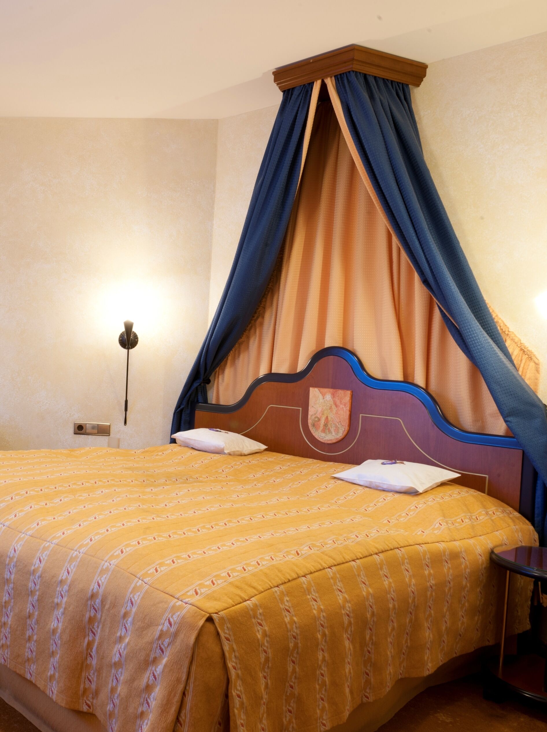 A hotel room with a bed, a nightstand, a wall-mounted lamp, and a curtain.