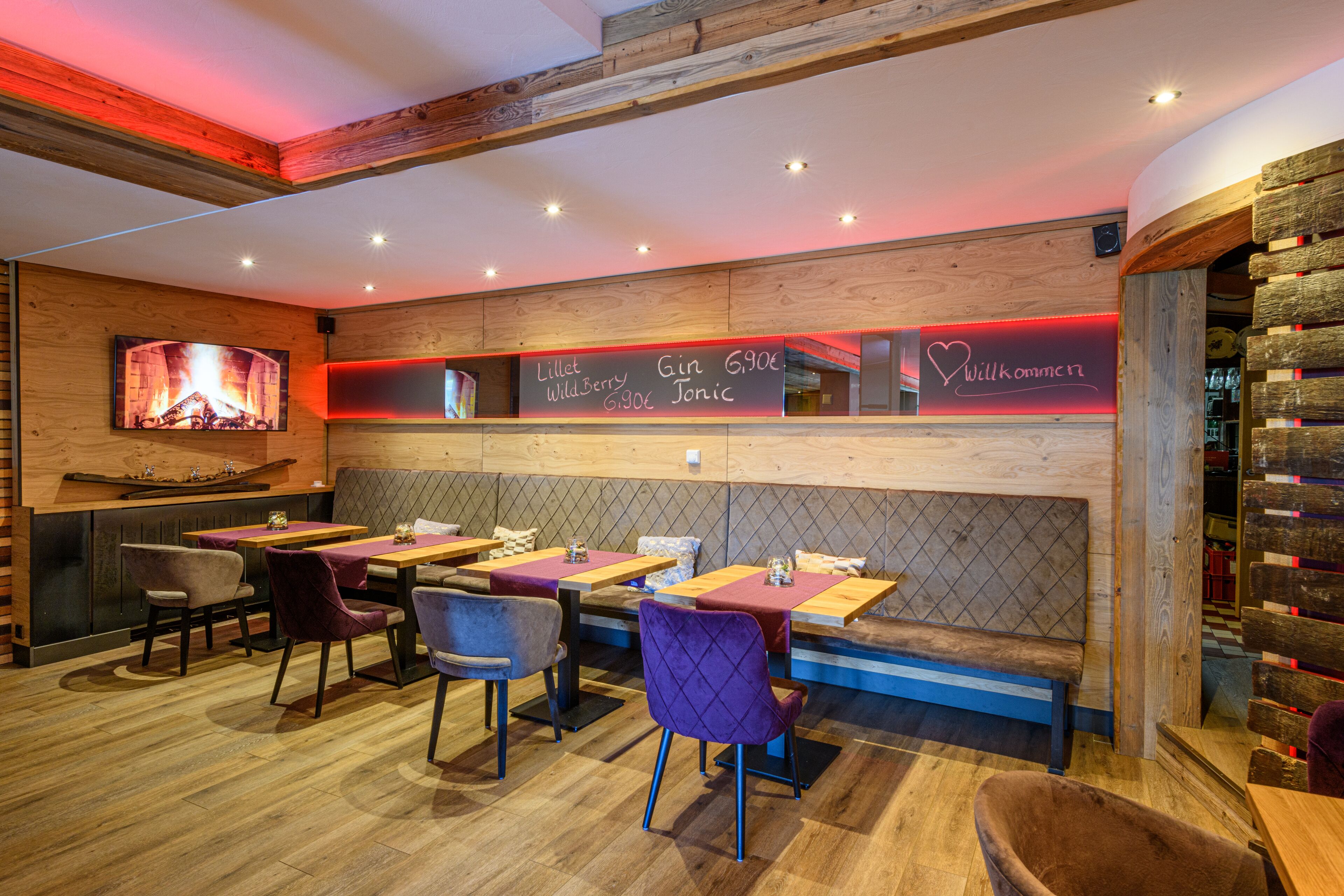 A restaurant with wooden walls, tables, and chairs. There is a menu board with drink options.