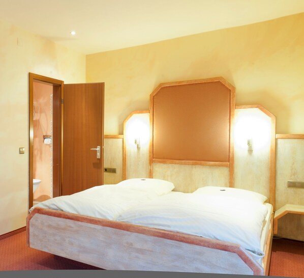 Una habitación de hotel con una cama grande, cabecera de madera y dos lámparas fijadas a la pared.