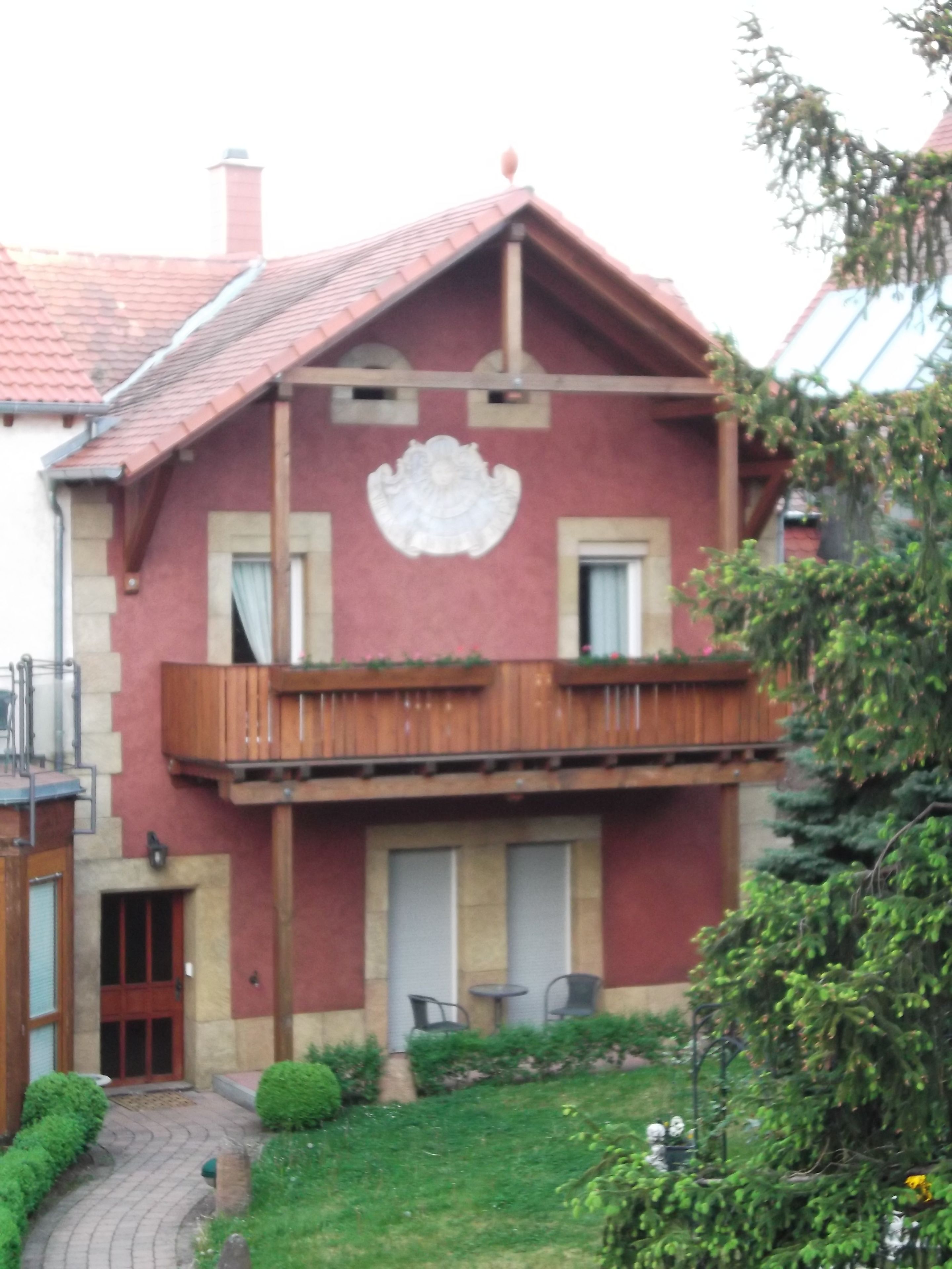 Une maison à deux étages avec une façade rouge, un balcon et un petit jardin.