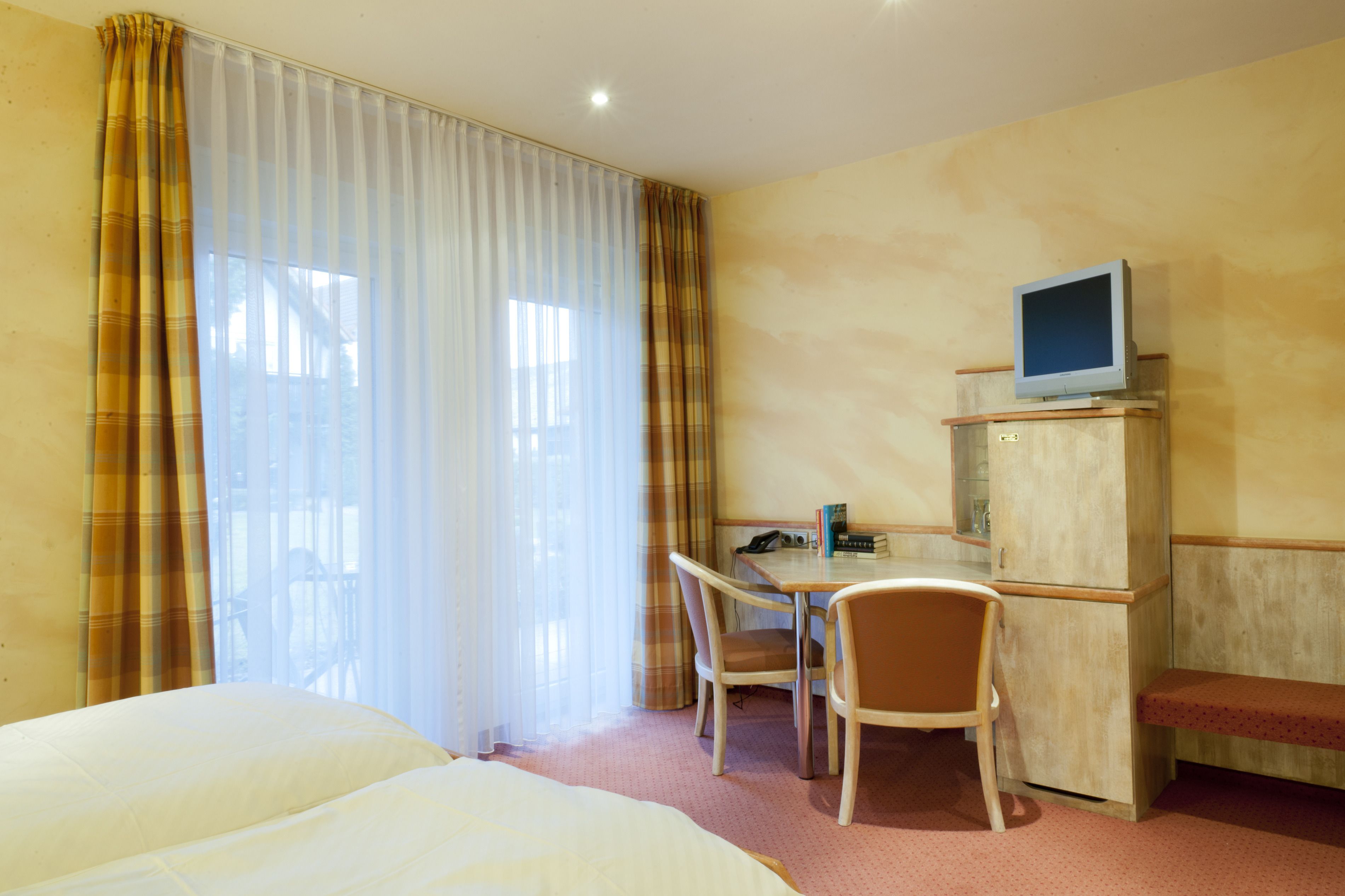 Habitación de hotel con dos camas, un escritorio con computadora, un televisor en un mueble y una silla.