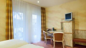 Habitación de hotel con dos camas, un escritorio con computadora, un televisor en un mueble y una silla.