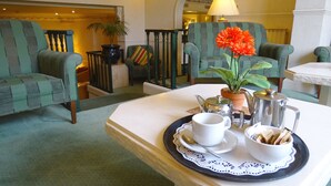 A cozy lounge area with green upholstered chairs, a white table with a tray of tea and a flower, and a potted plant. - La Trelade Hotel (St. Martins)