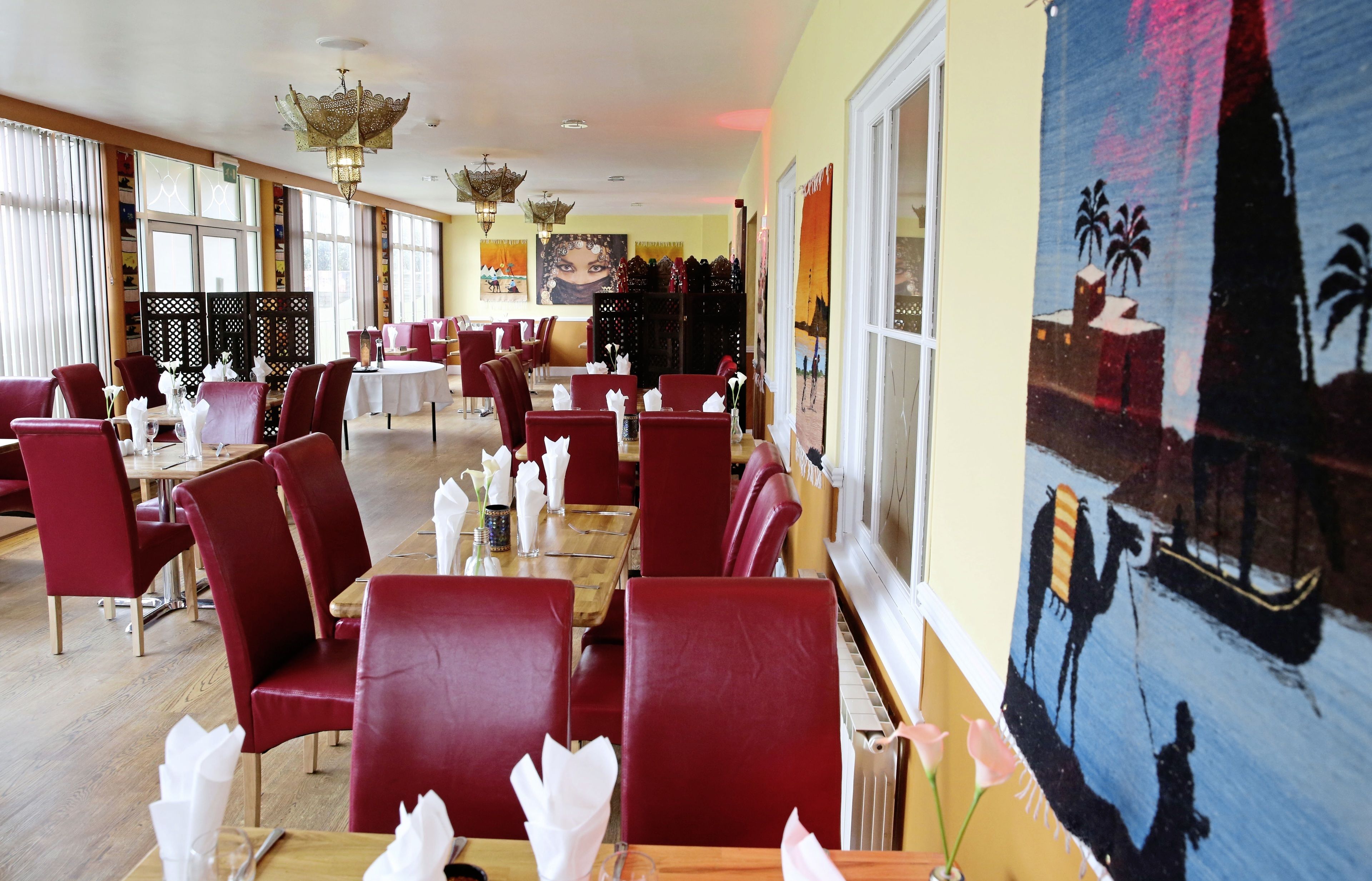 Un restaurant avec des chaises et des tables rouges, de grandes fenêtres et une fresque murale.