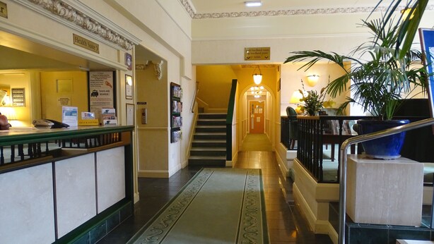A hotel reception area with a reception desk, a staircase, and a hallway leading to the upper floors. - La Trelade Hotel (St. Martins)