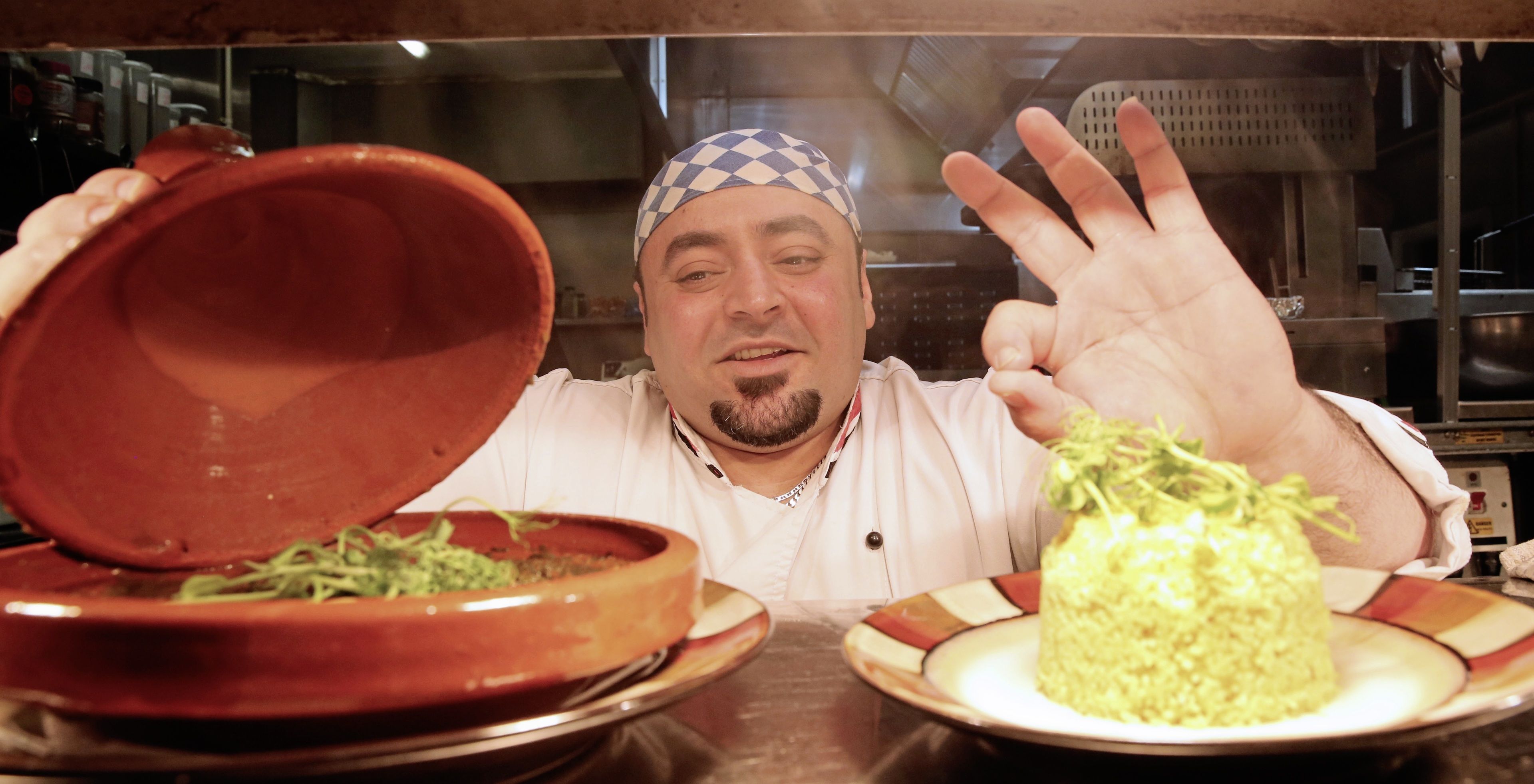 A chef in a kitchen with a clay pot and a plate of rice.