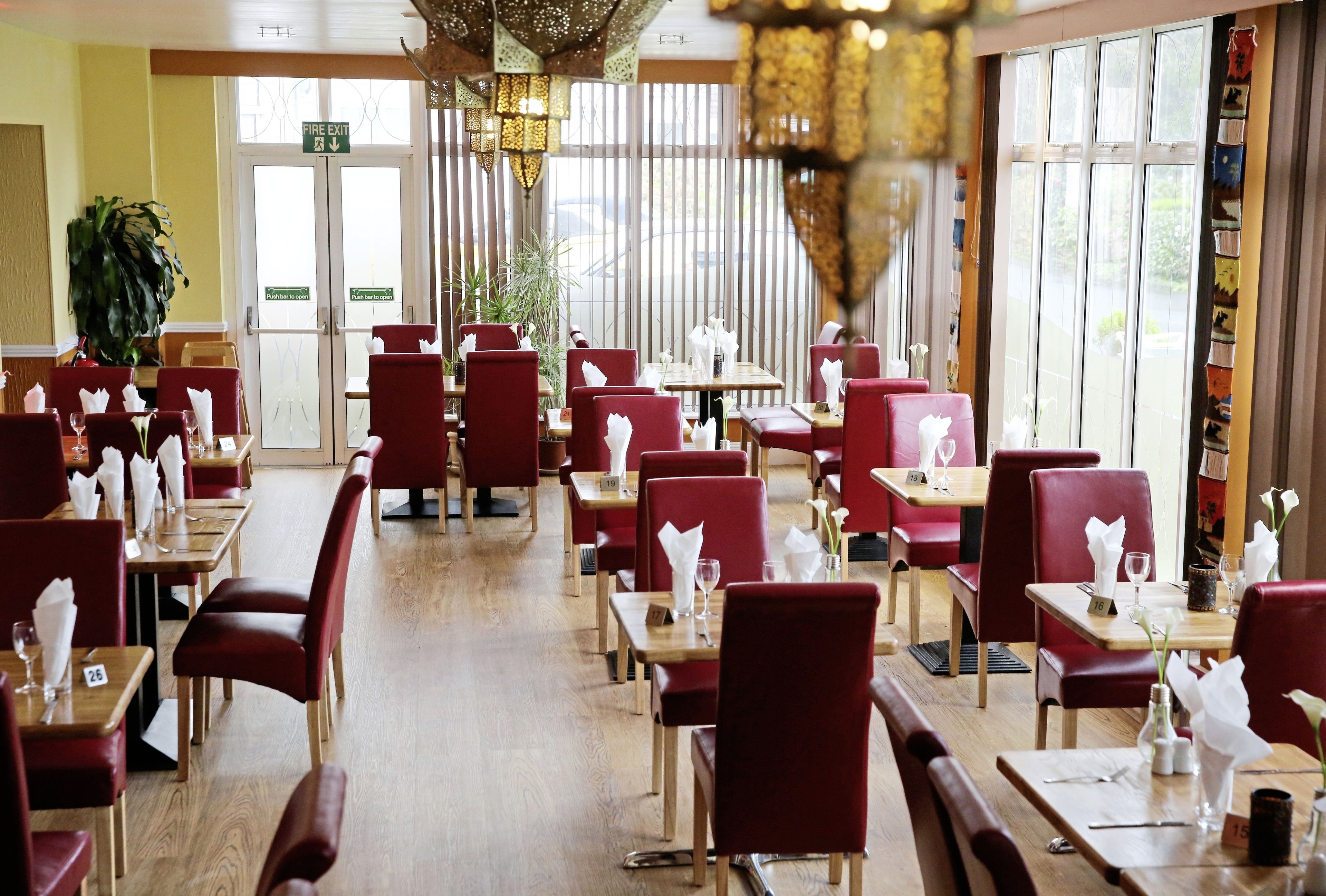 A restaurant with red upholstered chairs and wooden tables, arranged in a spacious layout with large windows allowing natural light.