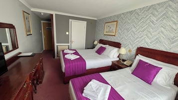 A hotel room with two beds, a wooden dresser, a mirror, and a herringbone-patterned wall.