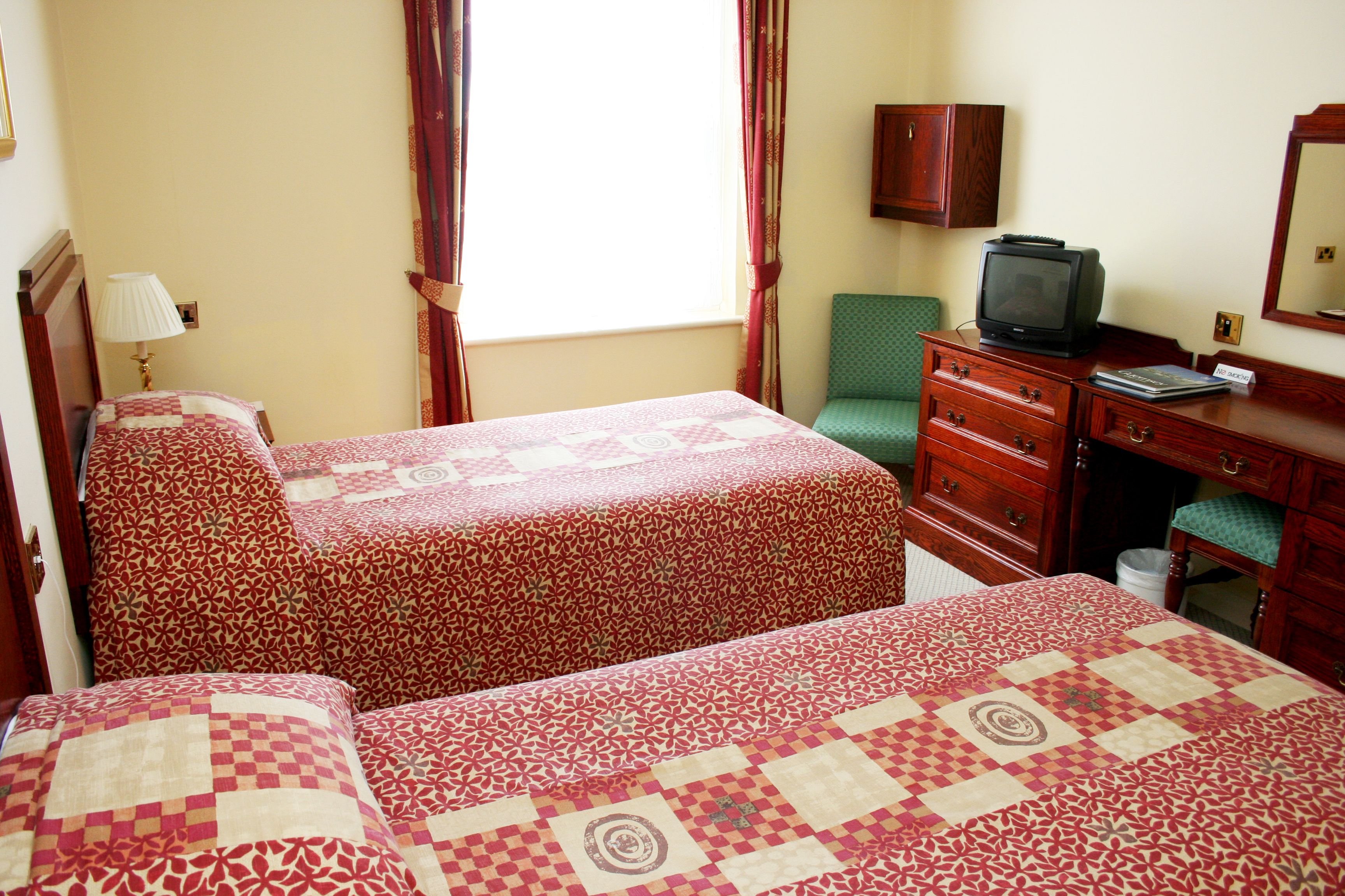 A hotel room with two beds, a desk with a television, a chair, and a cabinet.