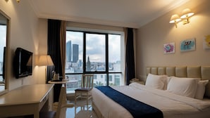 Ein Hotelzimmer mit Bett, Schreibtisch, Stuhl und einem großen Fenster mit Blick auf die Stadt.