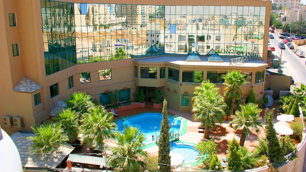 Das Amman West Hotel mit einem zentralen Innenhof, der einen Swimmingpool, Palmen und Sitzbereiche im Freien beherbergt.