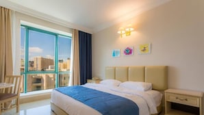 Ein Hotelzimmer mit einem großen Bett, einem Nachttisch, einem Sessel und einem Fenster mit Blick auf Gebäude.