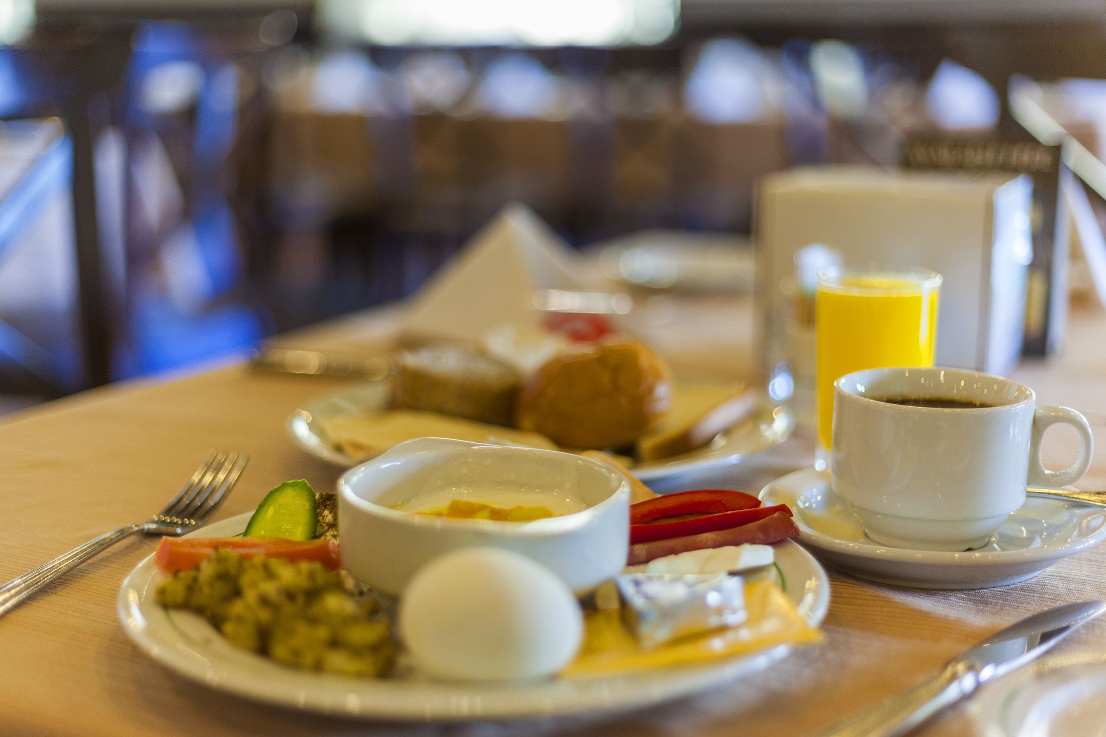 A breakfast setting with plates of food, a cup of coffee, and a glass of orange juice on a table.