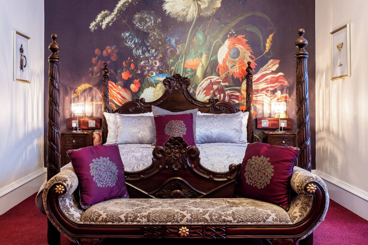A four-poster bed with ornate wooden headboard and footboard, flanked by two nightstands with lamps.