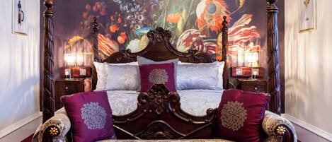 A four-poster bed with ornate wooden headboard and footboard, flanked by two nightstands with lamps.