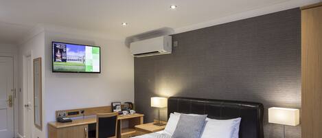 Habitación de hotel con cama, mesitas de noche, escritorio, televisor y aire acondicionado.