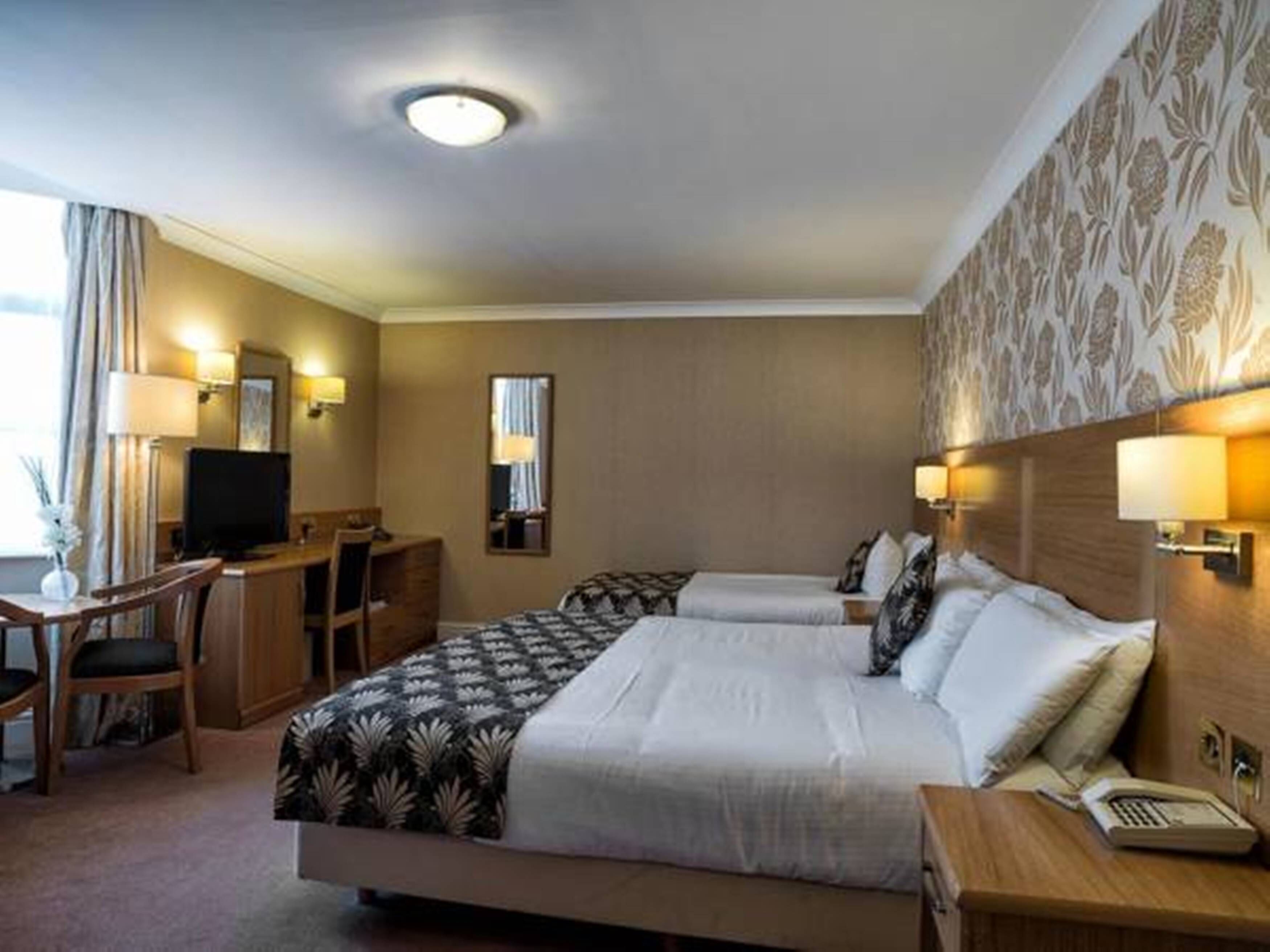 Ein Hotelzimmer mit zwei Betten, einem Schreibtisch, einem Fernseher und einem Telefon.