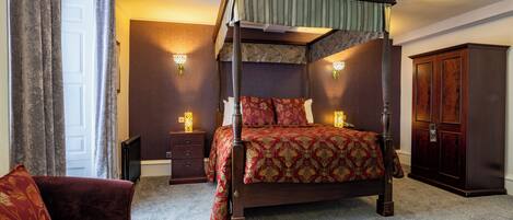 A four-poster bed with a canopy, a wooden nightstand, a dark wooden wardrobe, and a red upholstered armchair.