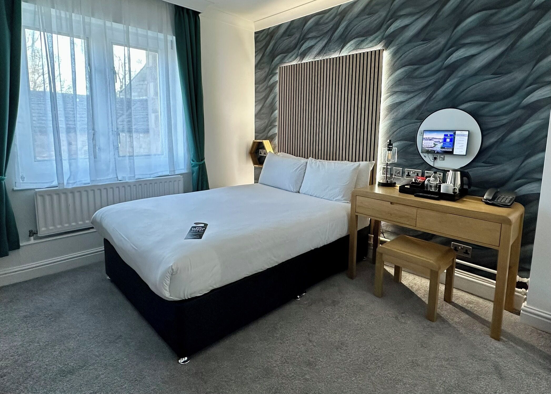 A hotel room with a bed, a desk, a chair, a lamp, a phone, and a TV.