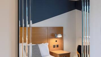 Una habitación de hotel moderna con cabecera de madera, mesita de noche con lámpara y una silla.