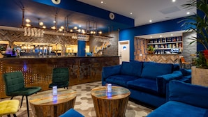 A bar area with a counter, bar stools, and a blue sofa. - Weetwood Hall Conference Centre & Hotel (Leeds)