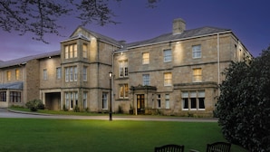 A large stone building with multiple windows and a well-maintained lawn. - Weetwood Hall Conference Centre & Hotel (Leeds)