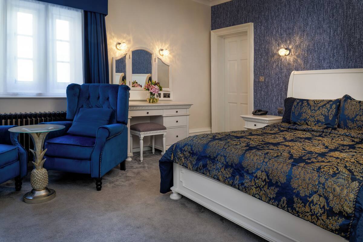 A bedroom with a large bed, a vanity with a mirror, a chair, and a small table.