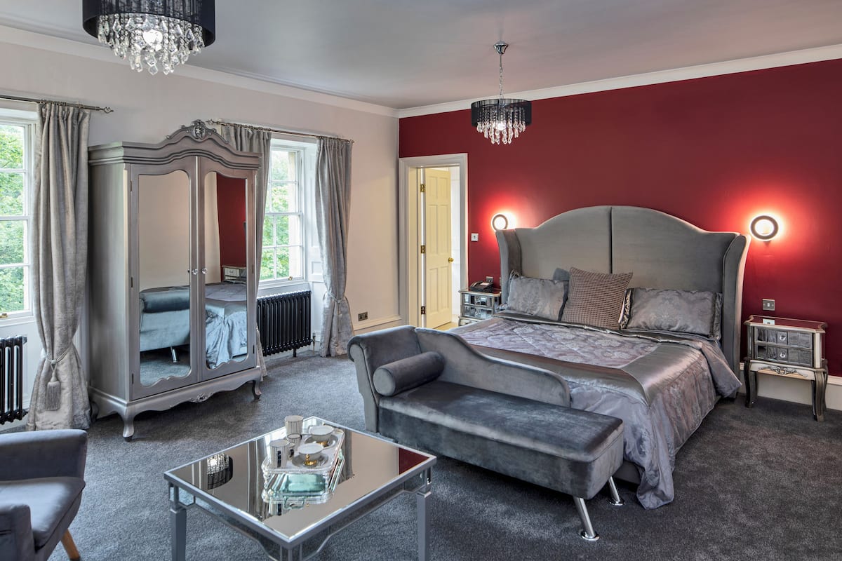A bedroom with a large bed, a chaise lounge, a glass coffee table, and a wardrobe.