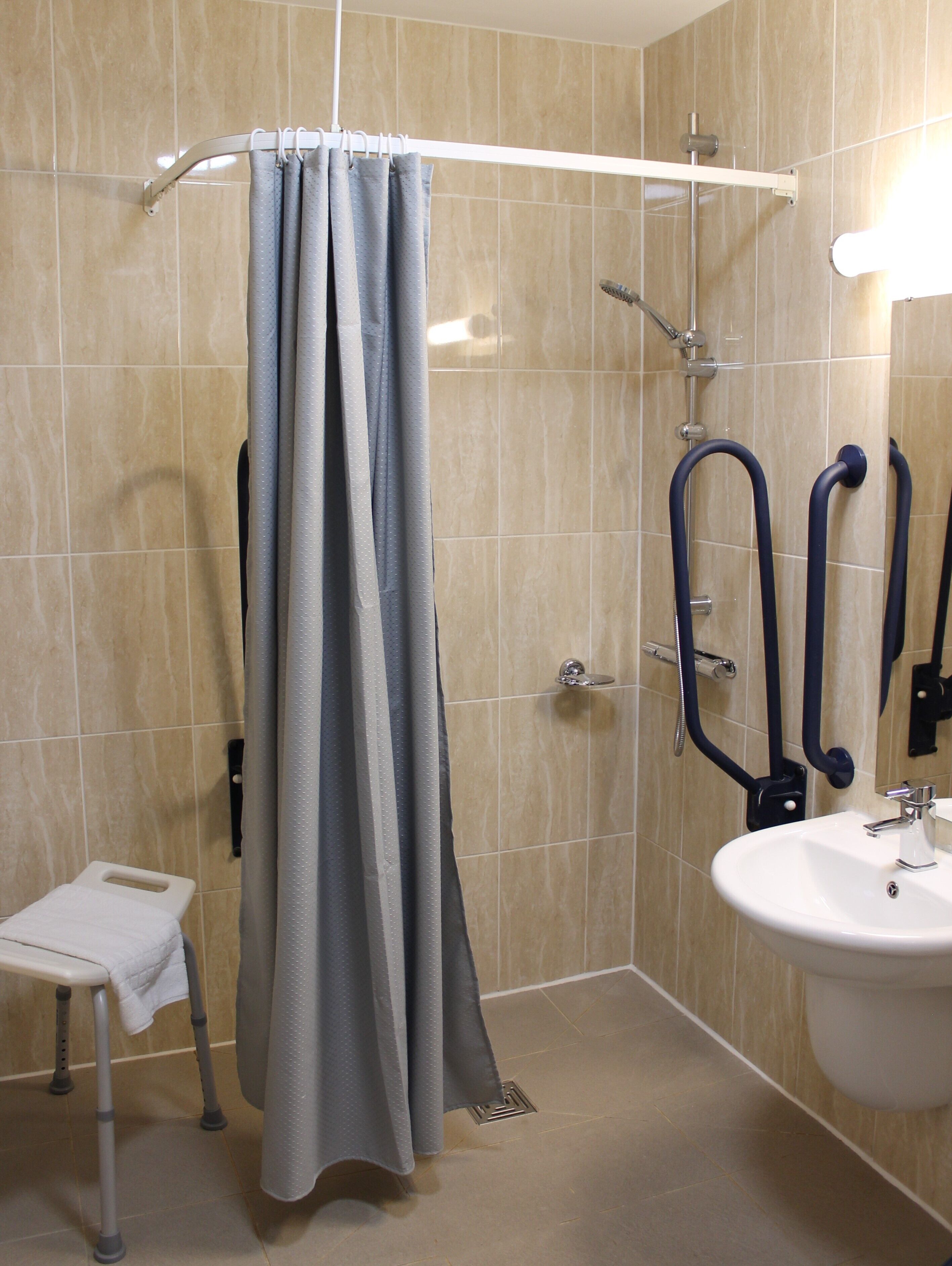 Un baño con ducha, lavabo y un pequeño taburete.