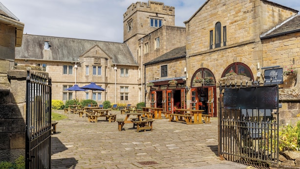 A courtyard with stone buildings, wooden tables, and benches. - Weetwood Hall Conference Centre & Hotel (Leeds)