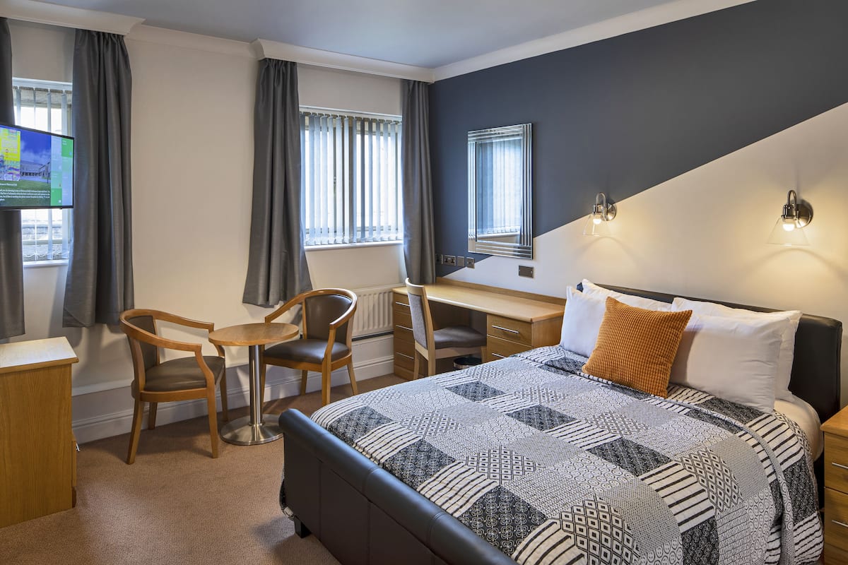 A hotel room with a bed, desk, and two chairs.