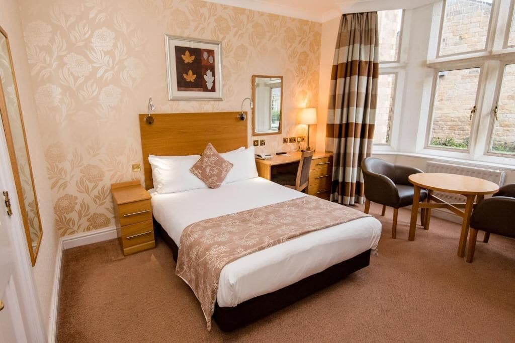 A hotel room with a large bed, a desk, a chair, and a small table.
