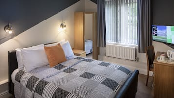 A bedroom with a bed, a desk, a chair, a TV, and a window with curtains.