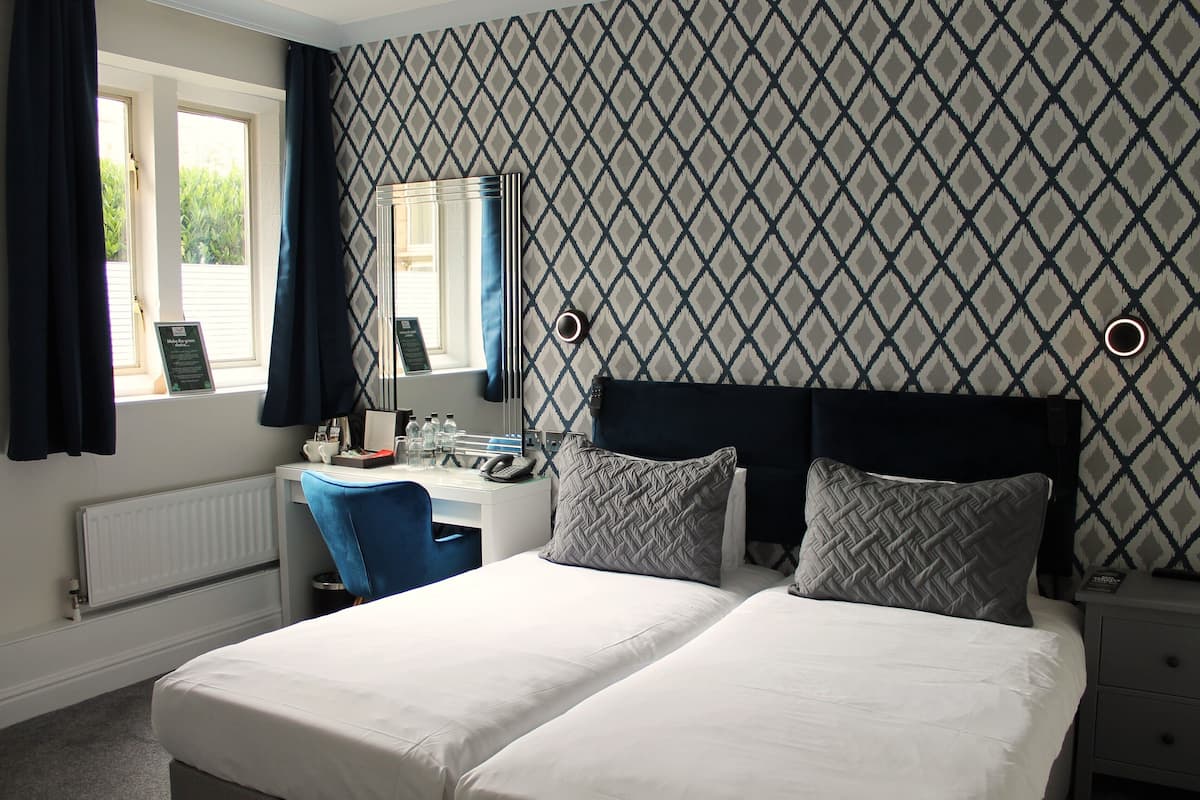 A hotel room with a large bed, a desk with a chair, a mirror, and a window with curtains.