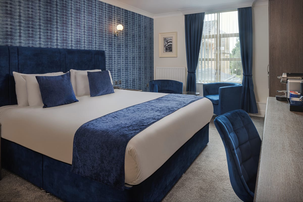 A hotel room with a large bed, a desk, a chair, and a view of the city through the window.