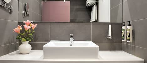 A modern bathroom with a white sink, a mirror, a towel rack, and a vase with flowers.
