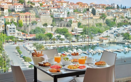 A table with breakfast items and a laptop, overlooking a marina and a hillside town.