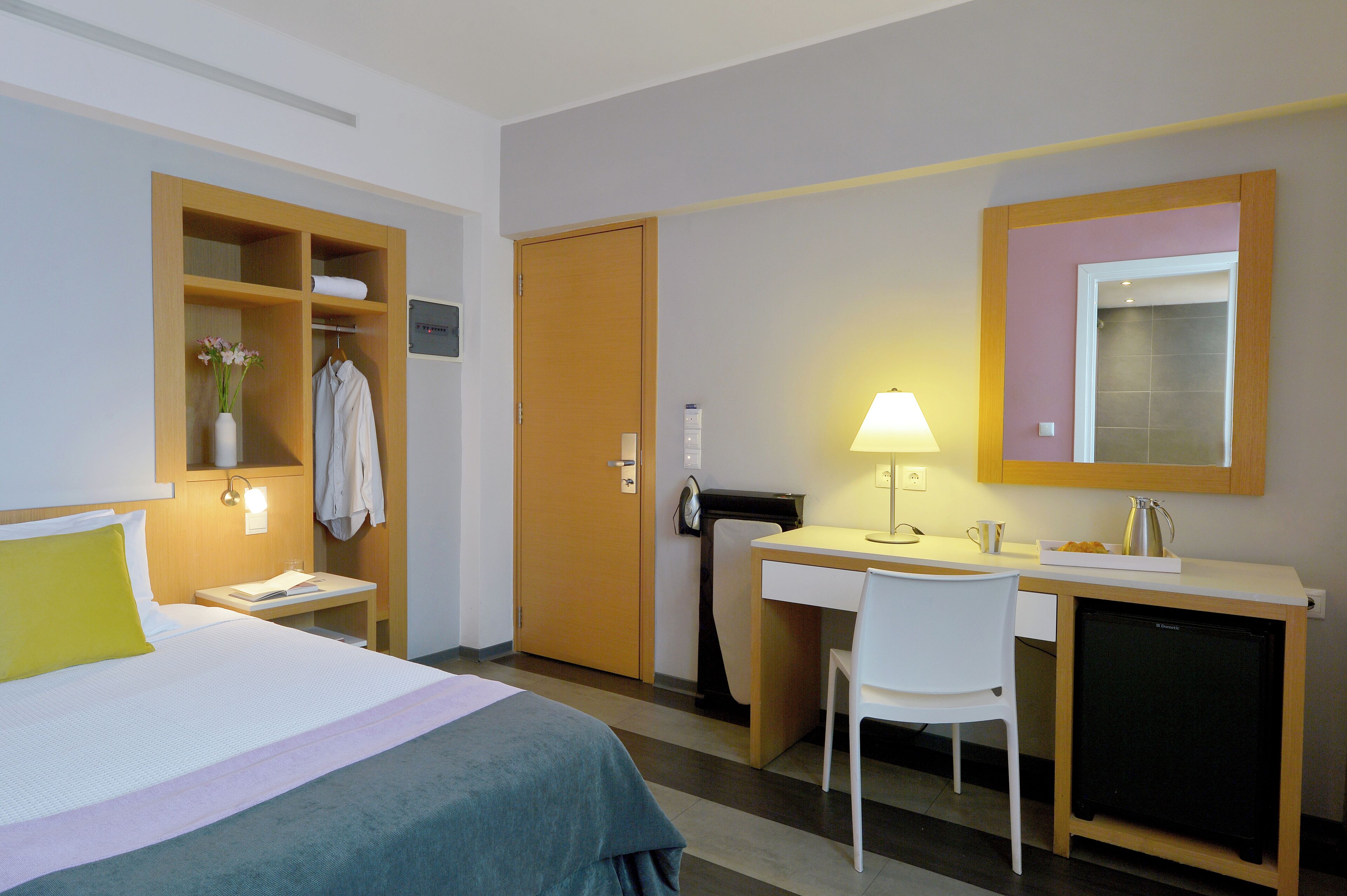A hotel room with a bed, desk, chair, and a small refrigerator.