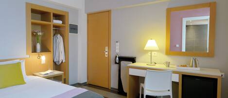 A hotel room with a bed, desk, chair, and a small refrigerator.
