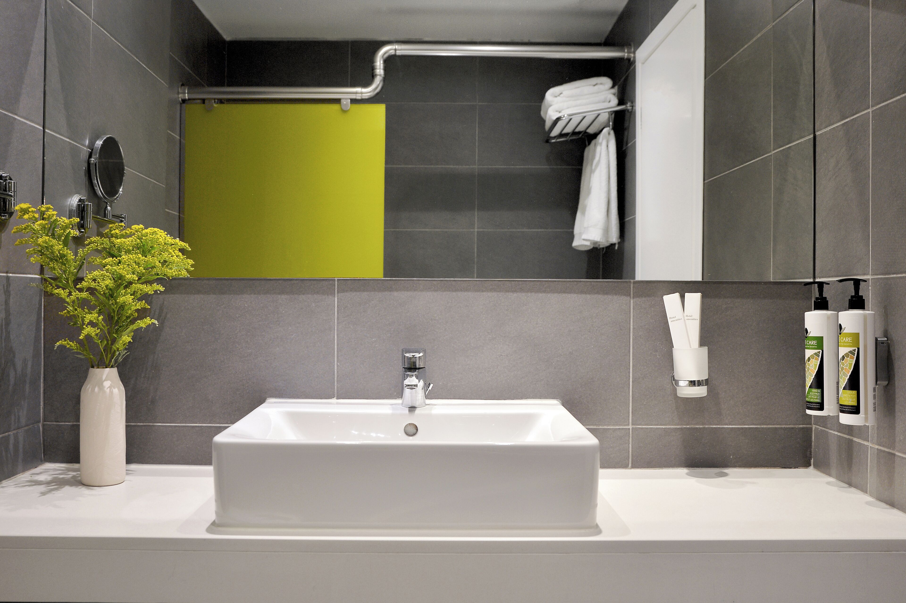 A modern bathroom with a white sink, grey tiles, a green shower curtain, and a towel rack with white towels.