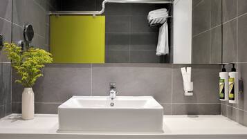 A modern bathroom with a white sink, grey tiles, a green shower curtain, and a towel rack with white towels.