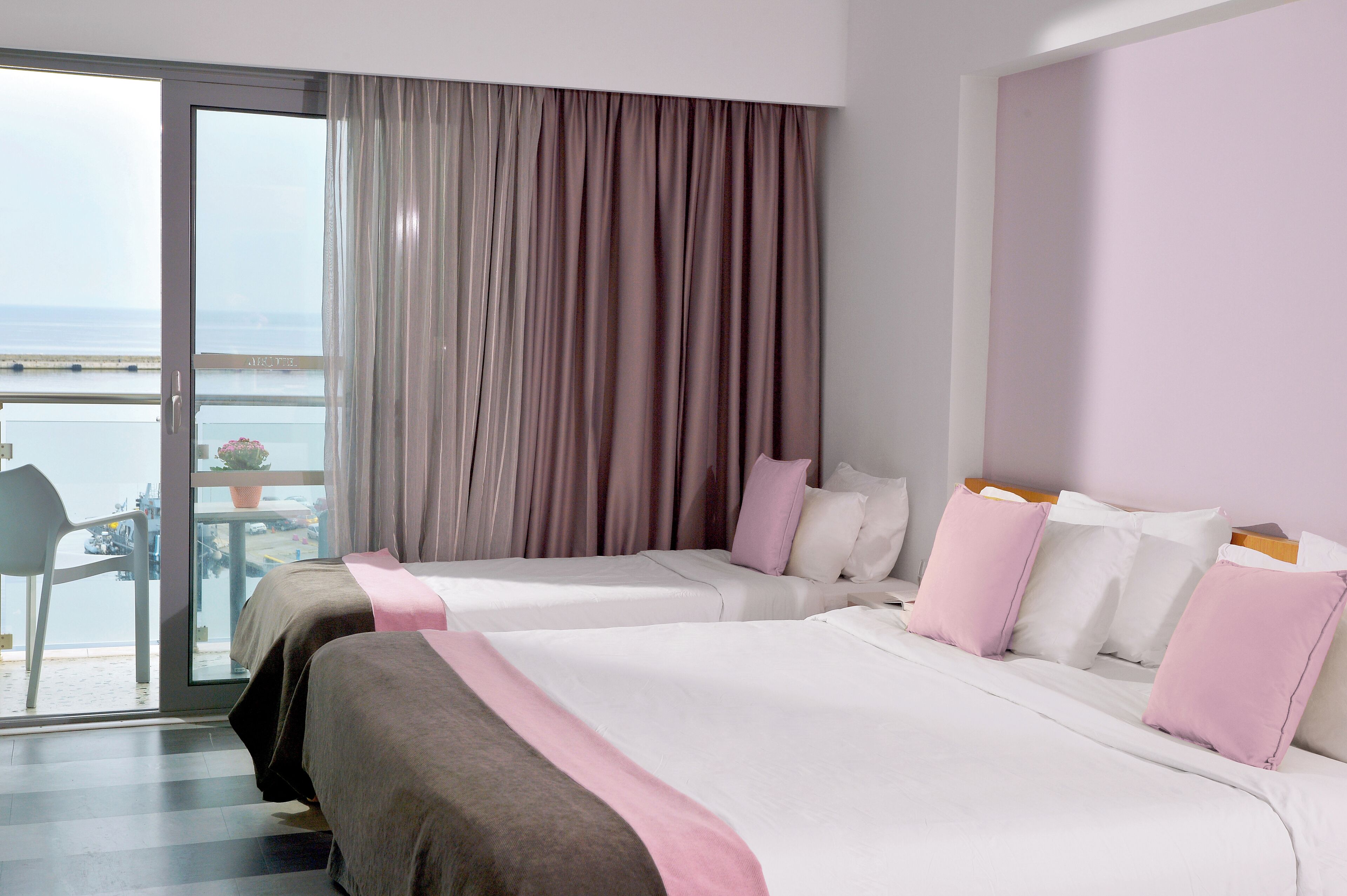 Habitación de hotel con dos camas, un balcón con vistas al mar y una mesa con sillas afuera.