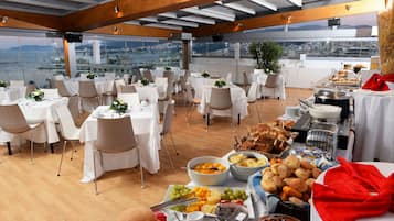 A rooftop dining area with tables set for a meal, a buffet with various food items, and a city view.