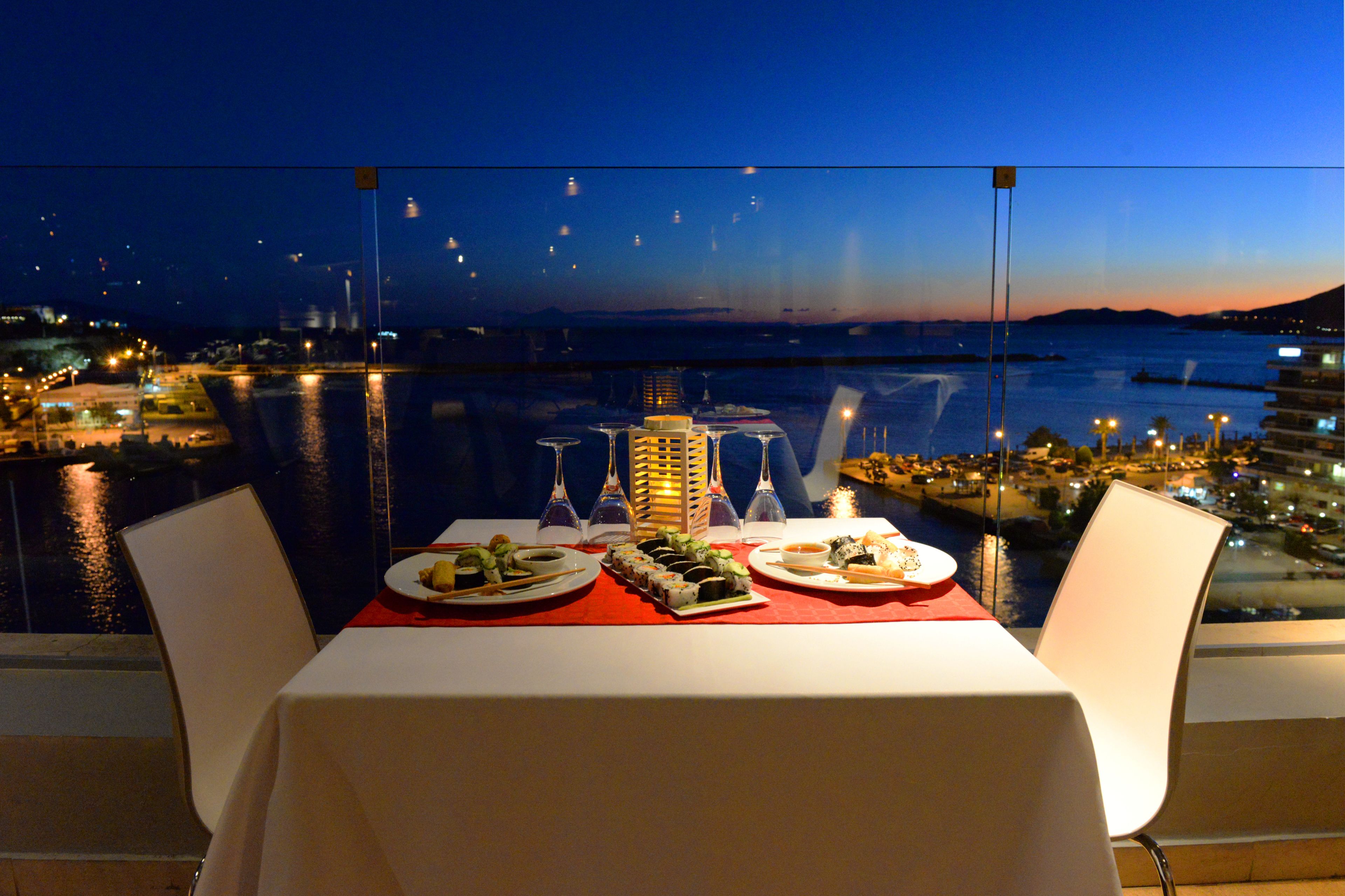 Mesa lista para la cena con vista a un paisaje urbano y al agua al atardecer.