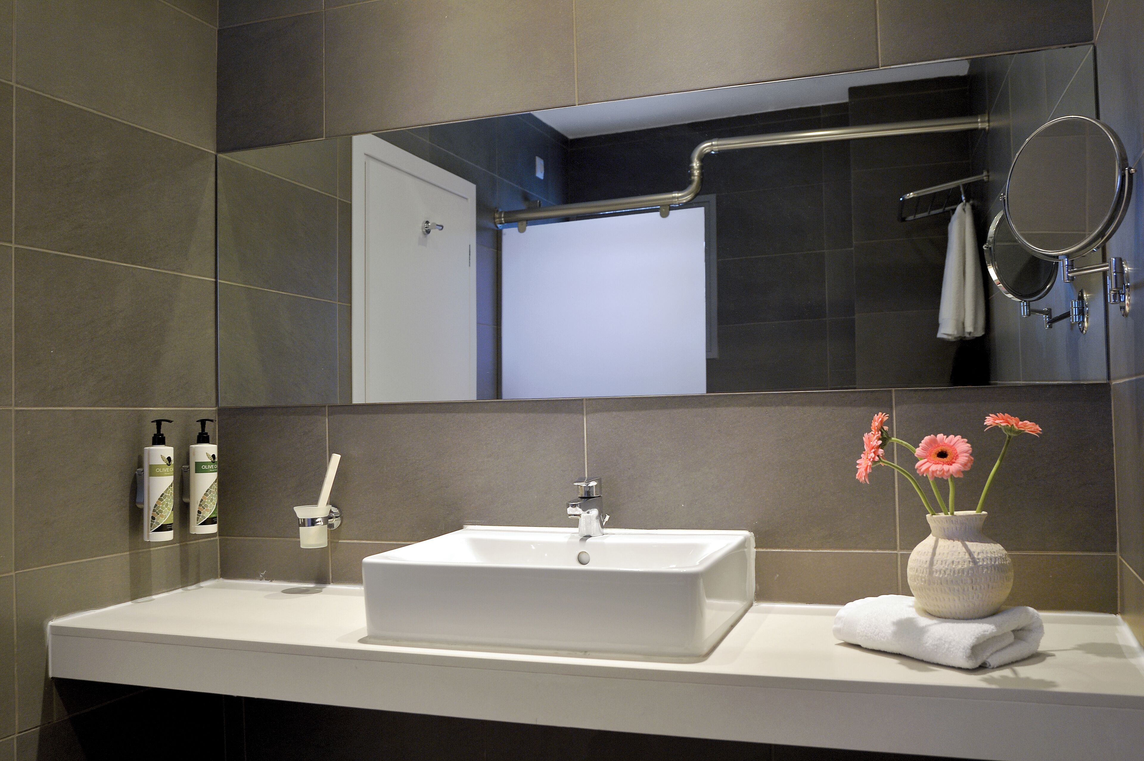 Un baño moderno con un lavamanos rectangular, un espejo y un florero con flores.