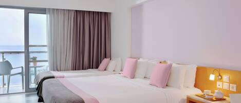 A hotel room with two beds, a small table with a tray of breakfast items, and a view of the sea through a large window.