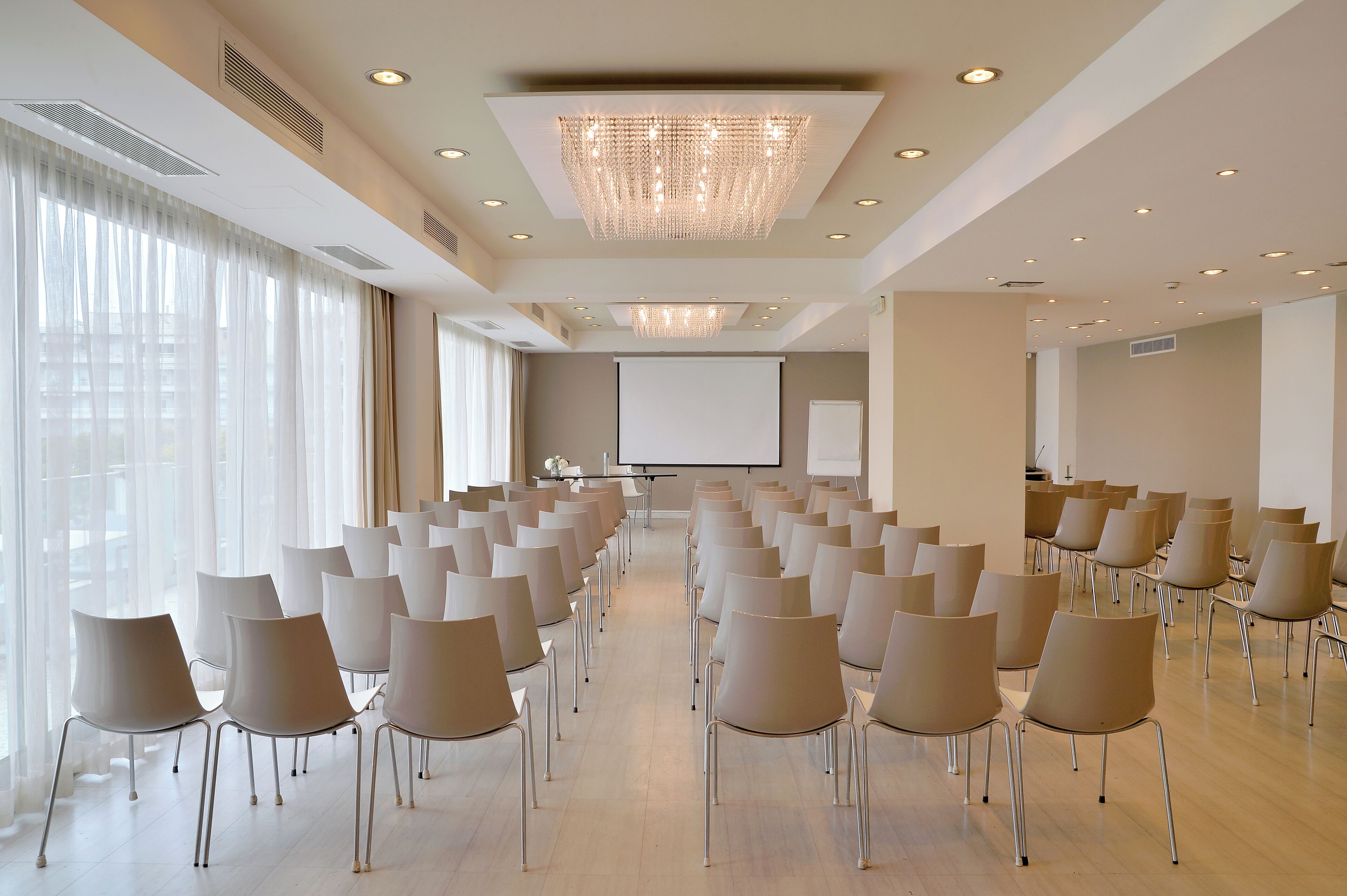 A conference room with rows of chairs, a projector screen, and a large chandelier.